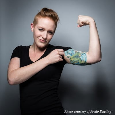 Beth flexes her left arm confidently displaying a tattoo depicting both model organisms she studies: frog and zebrafish