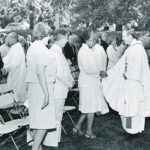 Father Monan in priestly robes shaking hands at a celebration